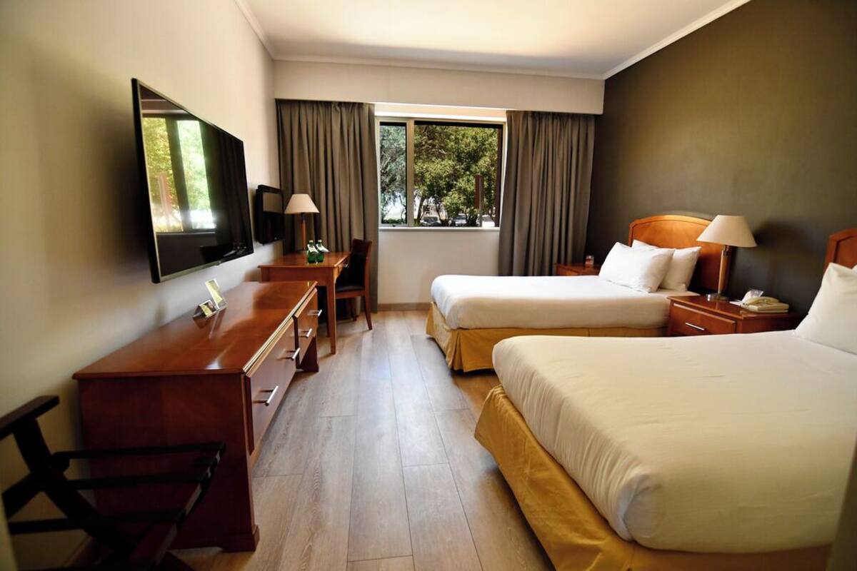 Een hotelkamer met twee bedden, een bureau, een televisie en een raam met gordijnen.
