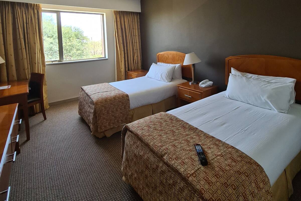 Een hotelkamer met twee bedden, een bureau, een stoel, een raam met gordijnen en een telefoon op het nachtkastje.