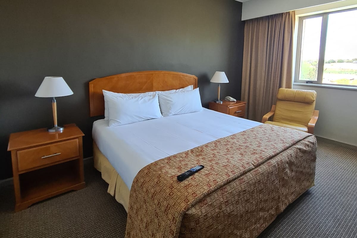 Een hotelkamer met een bed, twee nachtkastjes, een stoel, een raam en een plafondlamp.