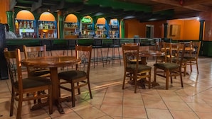 A restaurant interior with wooden tables and chairs, a bar area with bottles, and a green and orange color scheme. - Sunbird Mzuzu (Mzuzu)