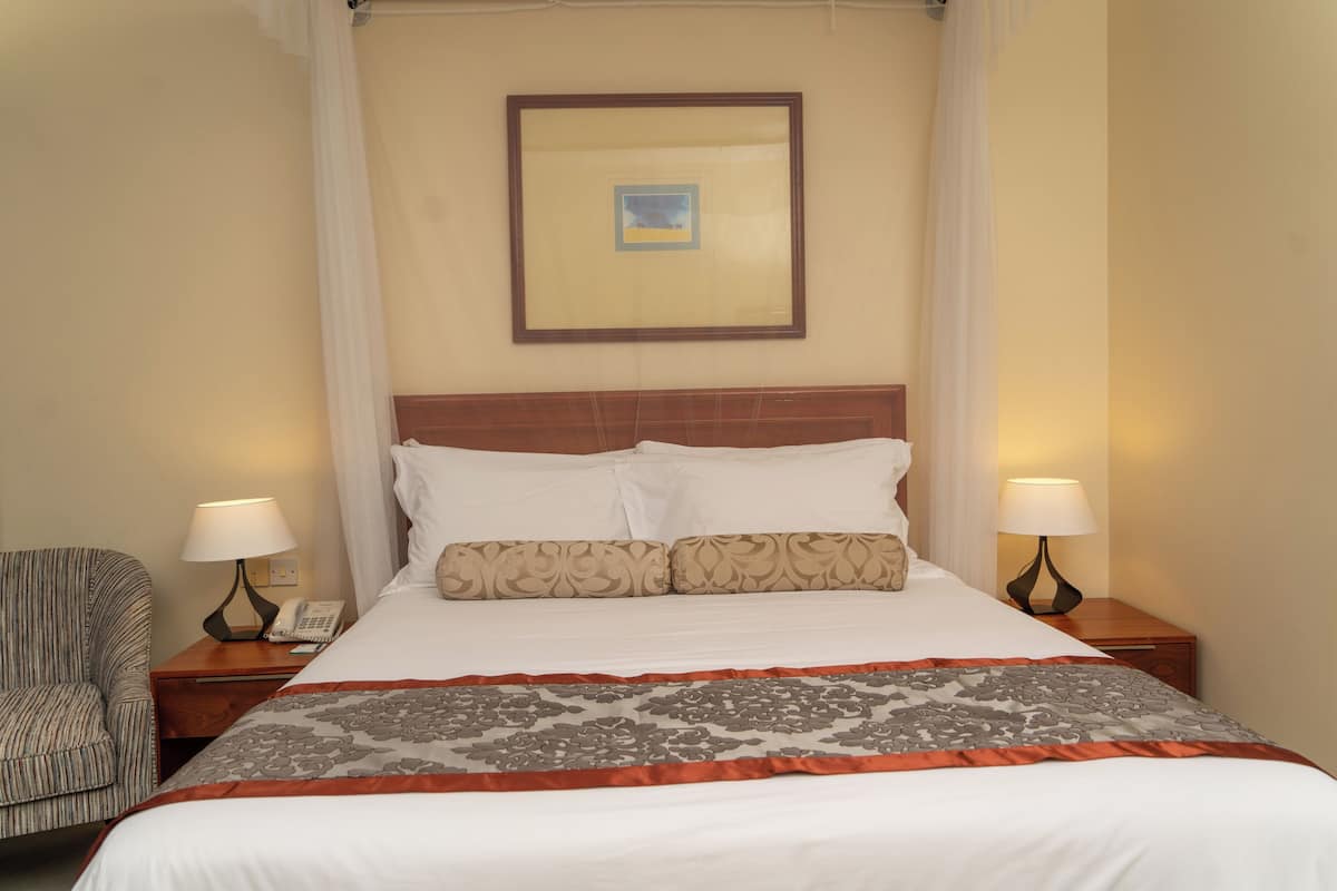A neatly made bed with a patterned bedspread, two bedside lamps, a telephone, and a chair.