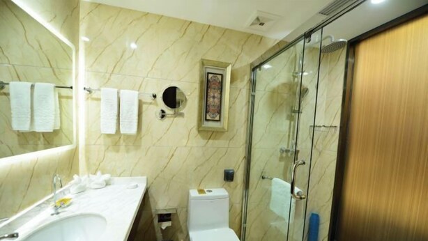 A bathroom with a marble wall, a sink, a toilet, and a glass shower enclosure. - Golden Lun Hotel (Lanzhou)