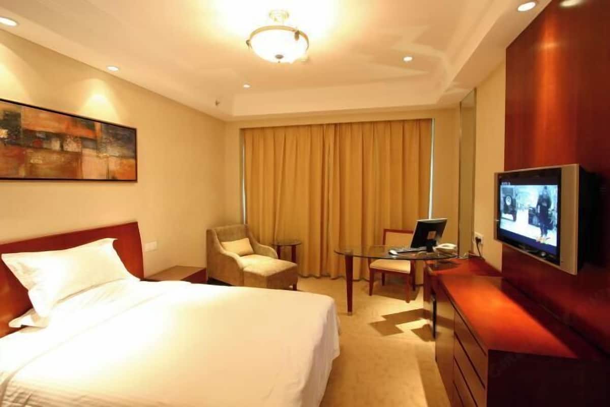 A hotel room with a bed, a desk with a laptop, a television, and a painting on the wall.