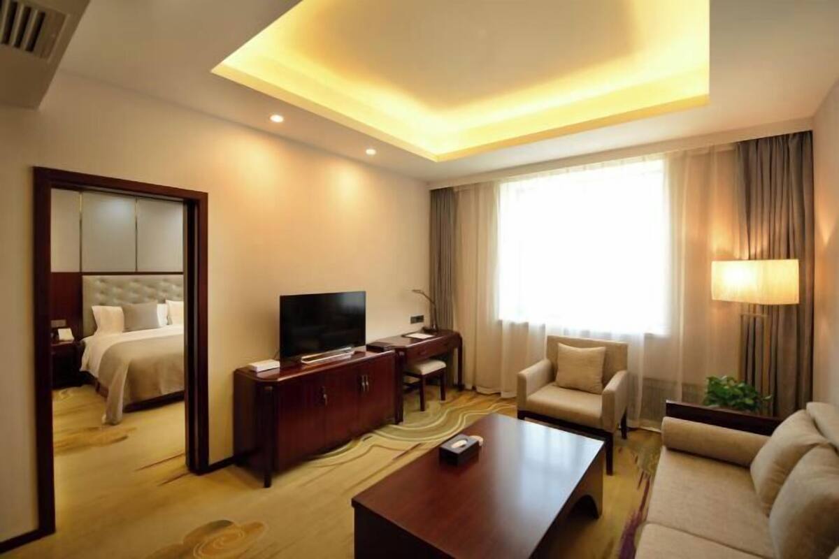 A hotel room with a bed, a TV, a desk, a sofa, and a large window.