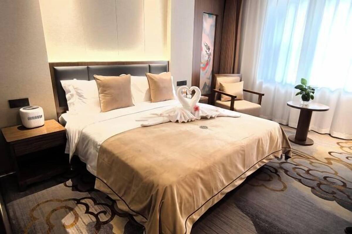 A hotel room with a bed, a nightstand, a chair, a small table, and a potted plant.