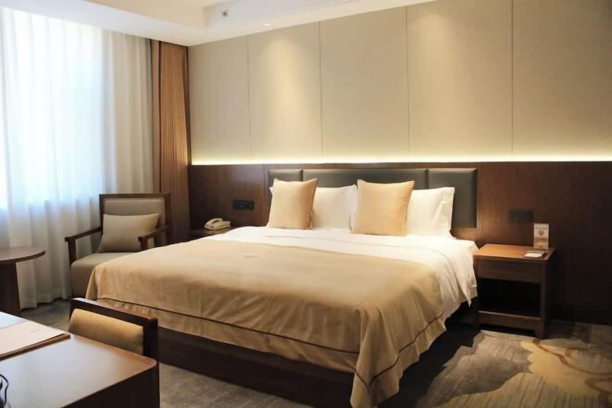 A hotel room with a large bed, bedside tables, a chair, and a desk.