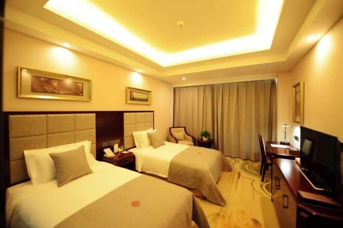 A hotel room with two beds, a desk with a TV, a chair, and a window with curtains.