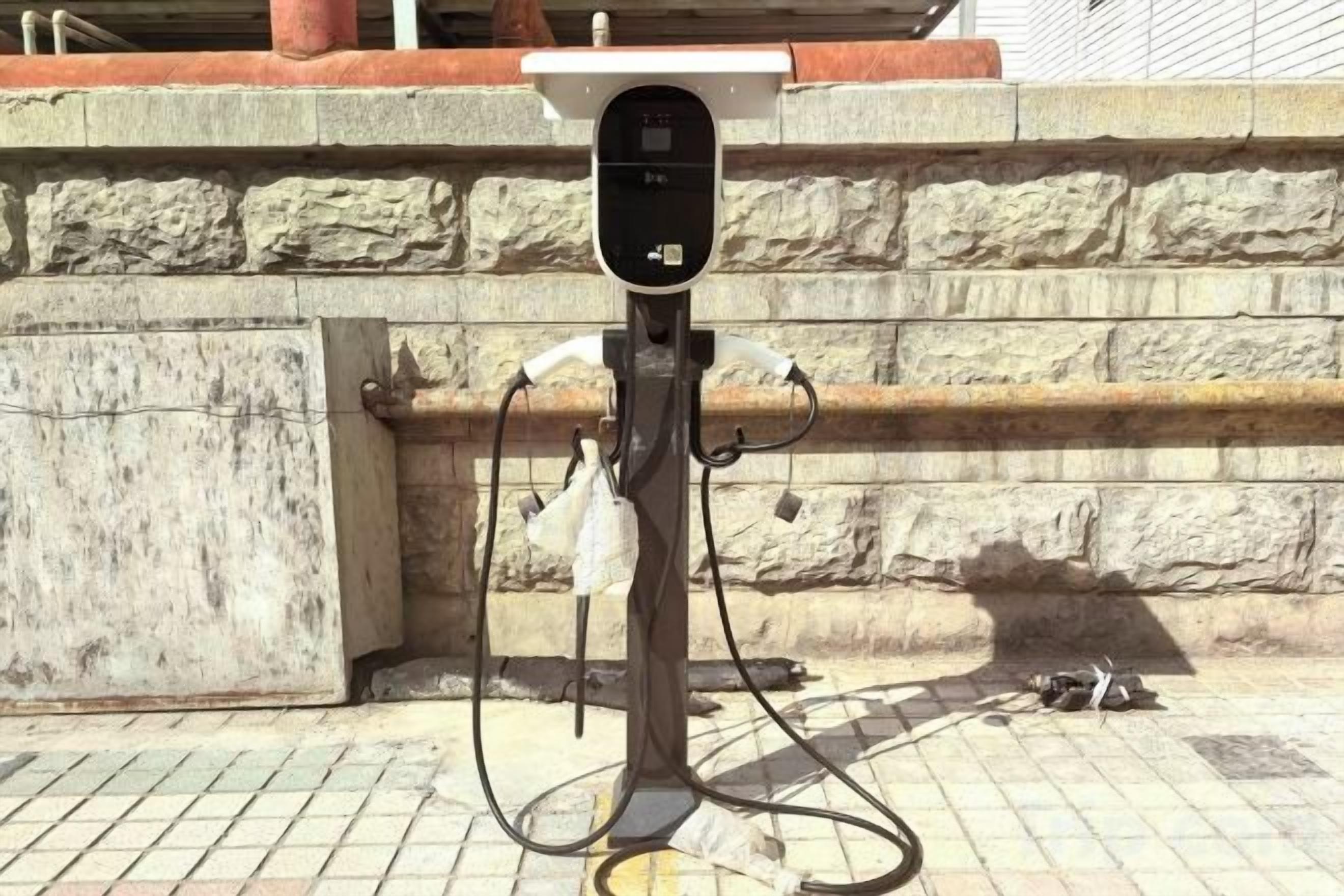 Una estación de carga portátil para vehículos eléctricos, con pantalla digital, sobre un fondo de pared de piedra.