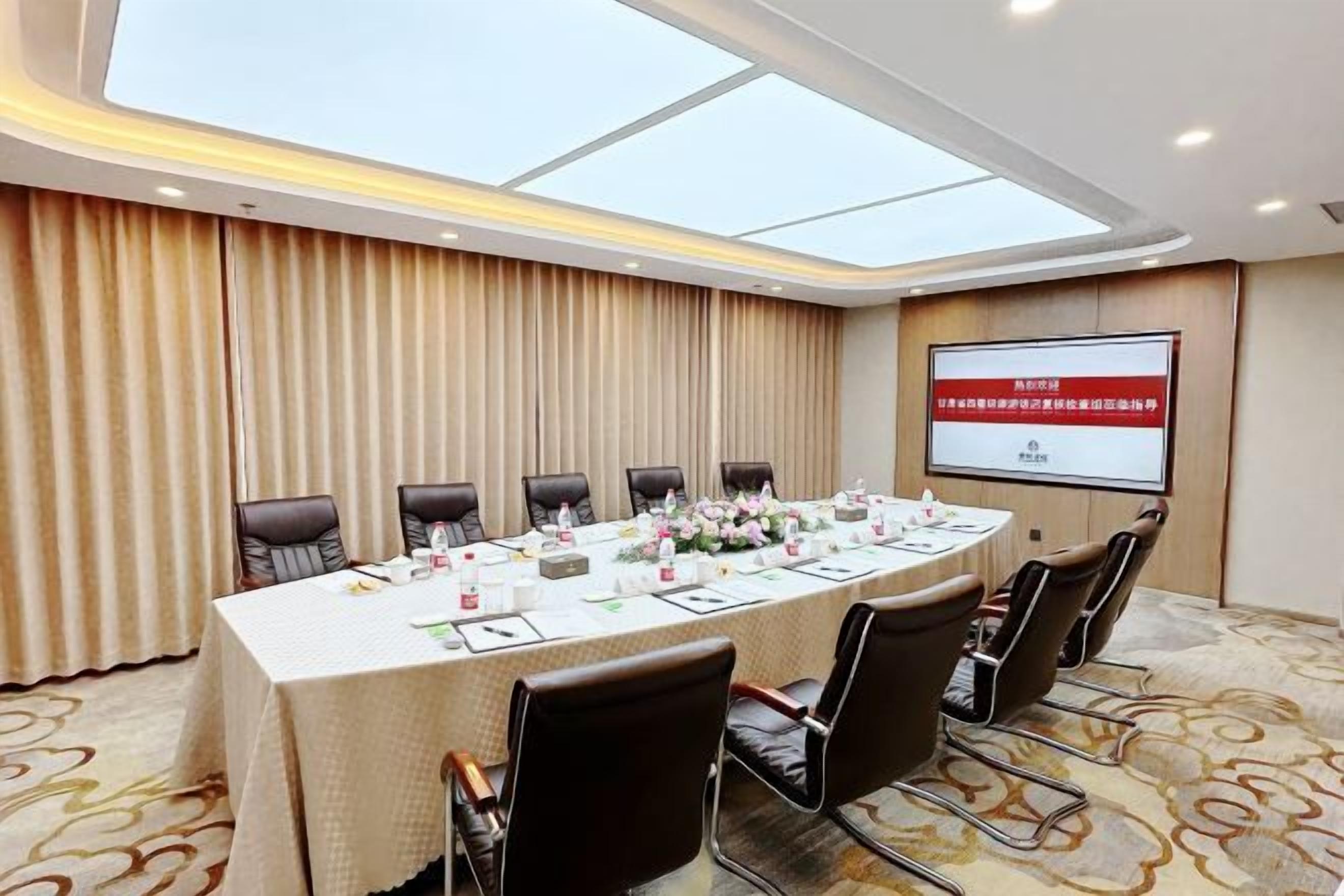 A conference room with a long table, chairs, a projector screen, and a large window.