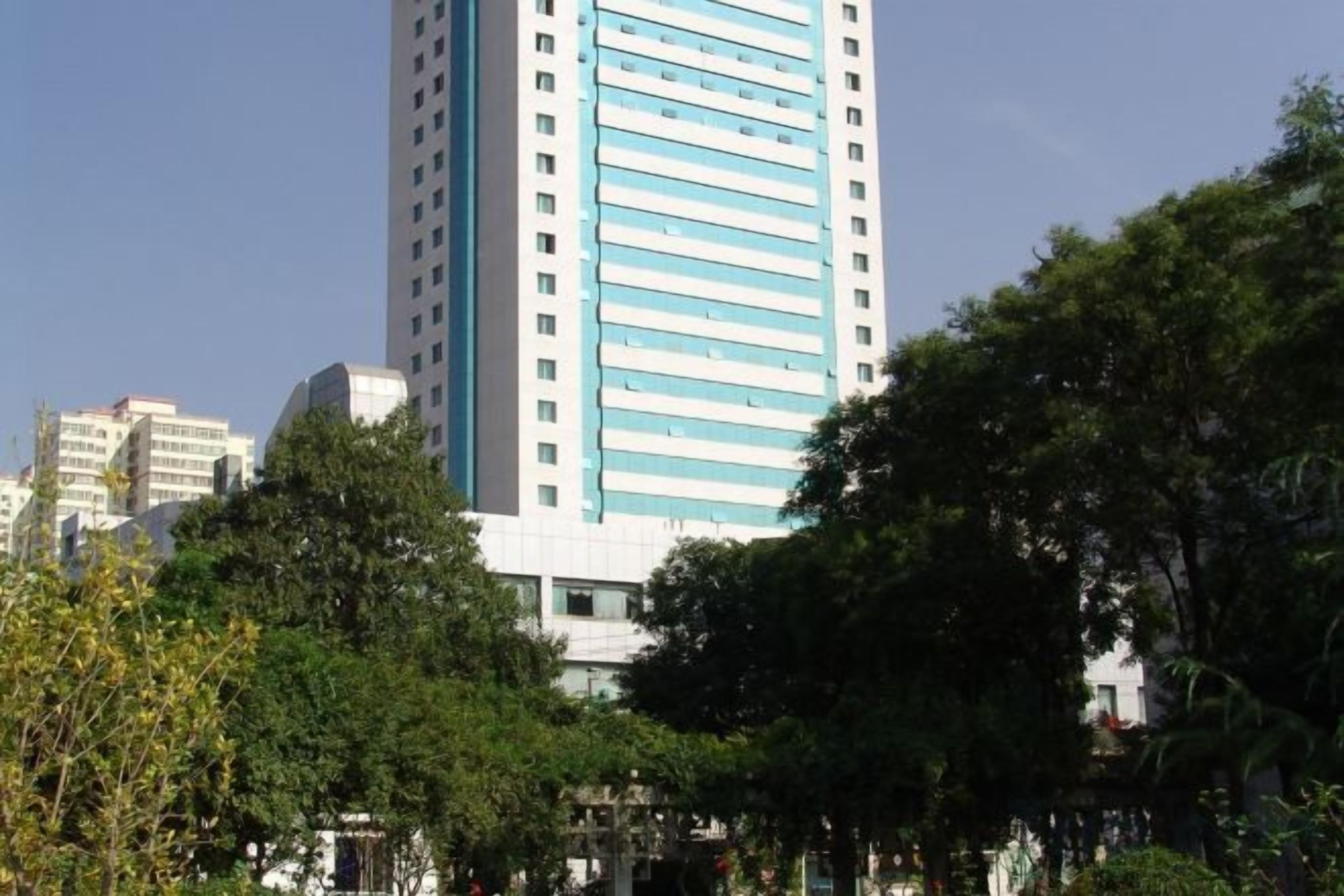 A tall building with a blue and white facade, surrounded by trees and other buildings.