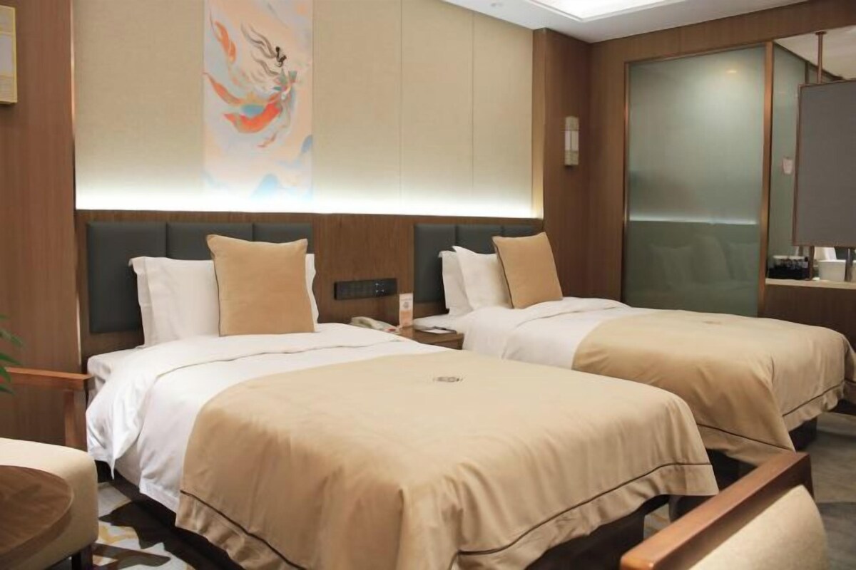 A hotel room with two beds, a large window, a painting on the wall, and a wooden headboard.