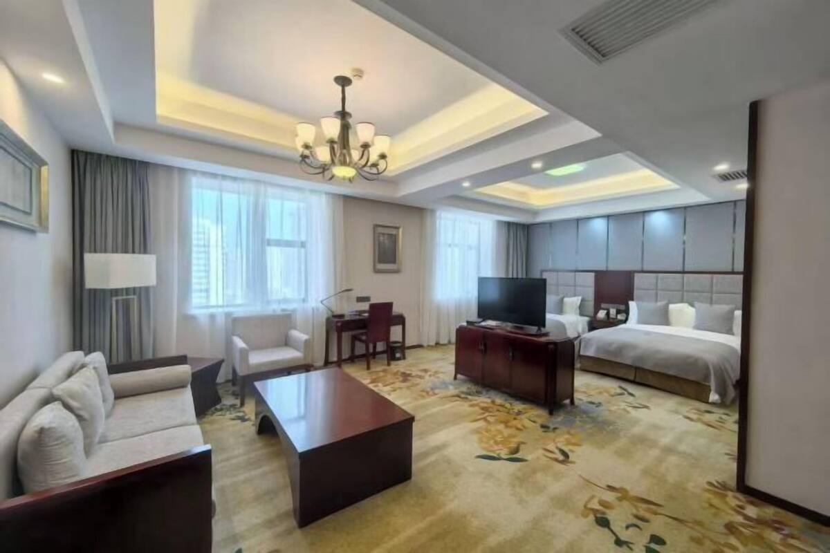 A hotel room with a sofa, a coffee table, a TV, a bed, and a desk.