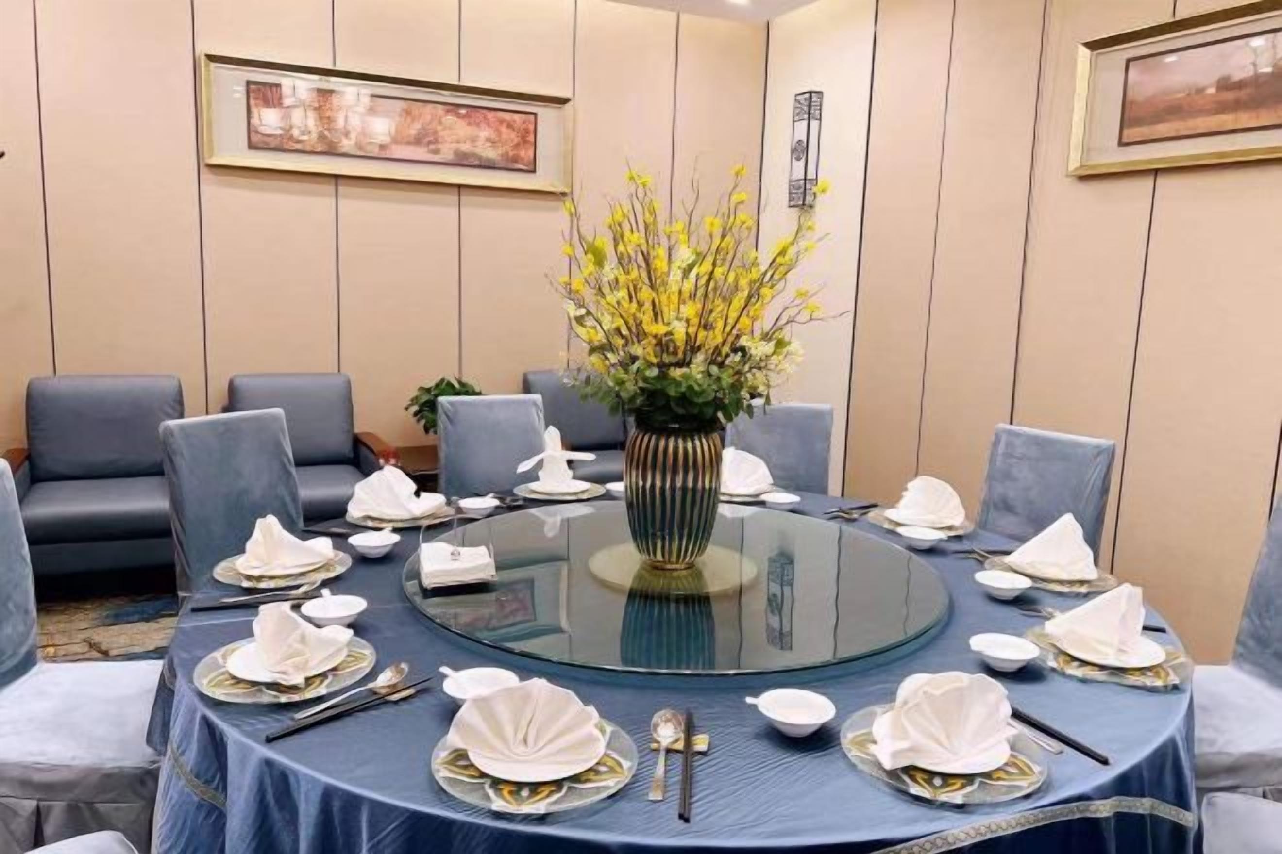 Una mesa redonda con cubierta de vidrio, rodeada de sillas y un florero con flores amarillas.
