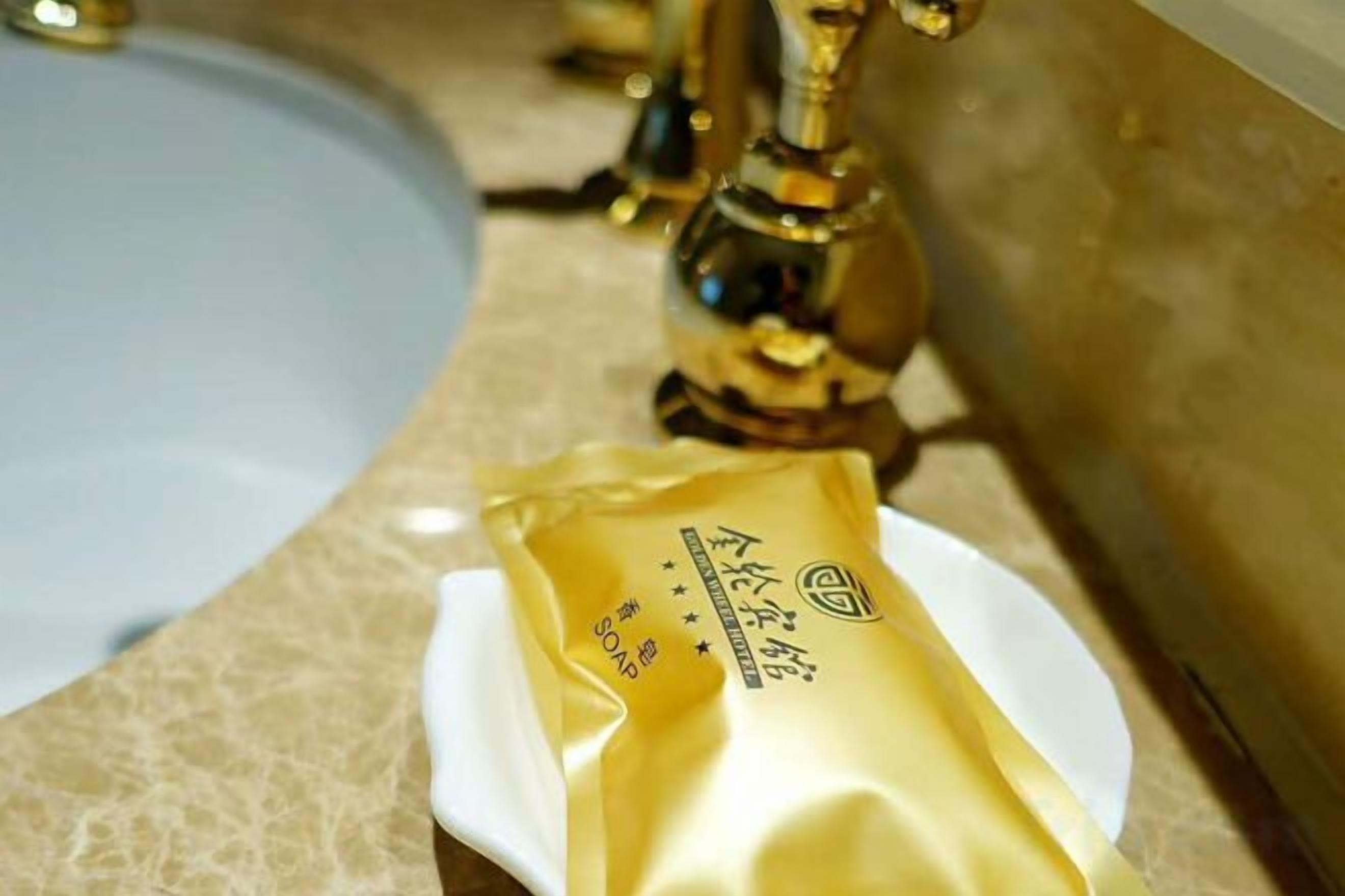 Ein Waschbecken mit goldenem Wasserhahn und ein weißer Teller mit einer goldenen Verpackung darauf.