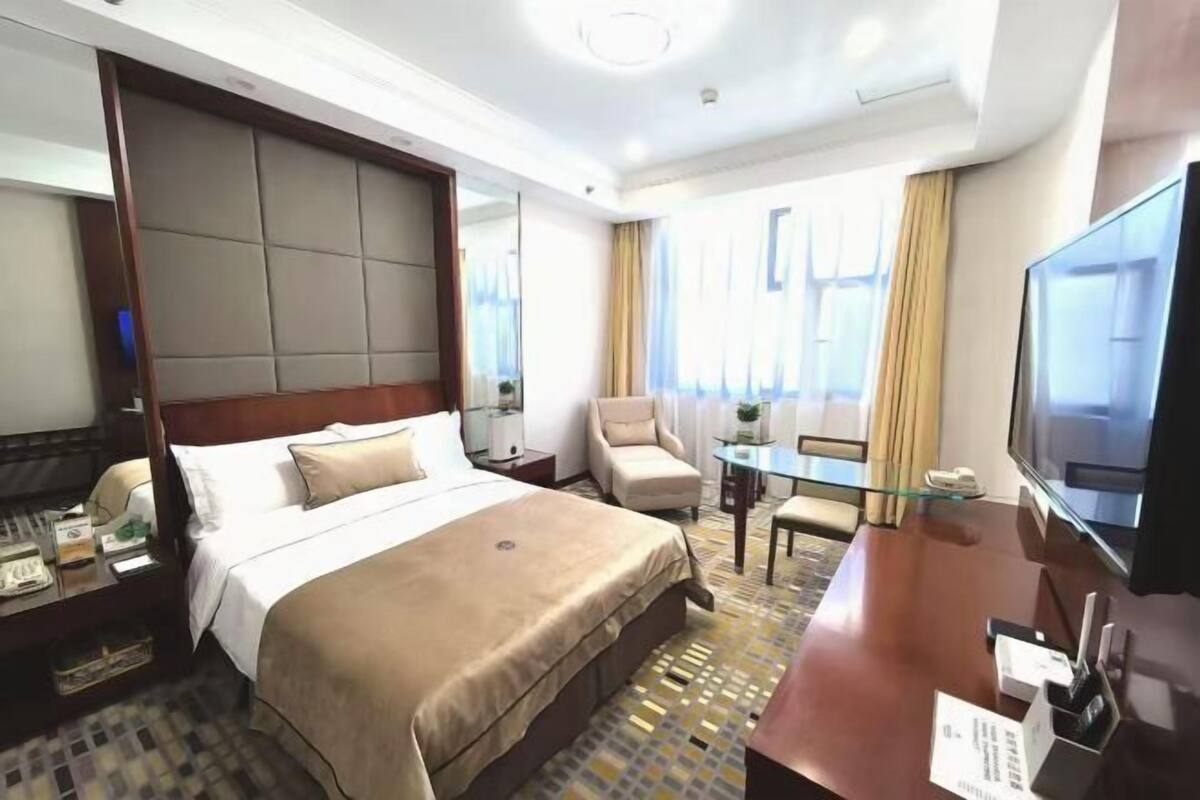 A hotel room with a large bed, a desk, a chair, a television, and a window with curtains.