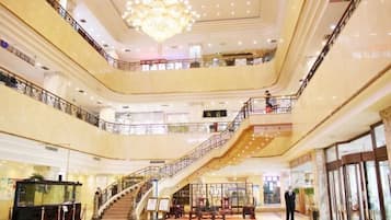 Un atrio de varios niveles con una gran escalera, barandillas de cristal y un candelabro.