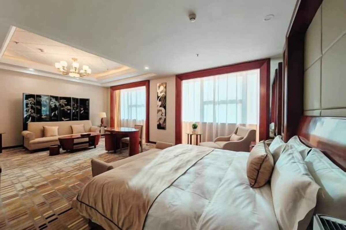 A hotel room with a large bed, a sofa, a dining table, and artwork on the walls.