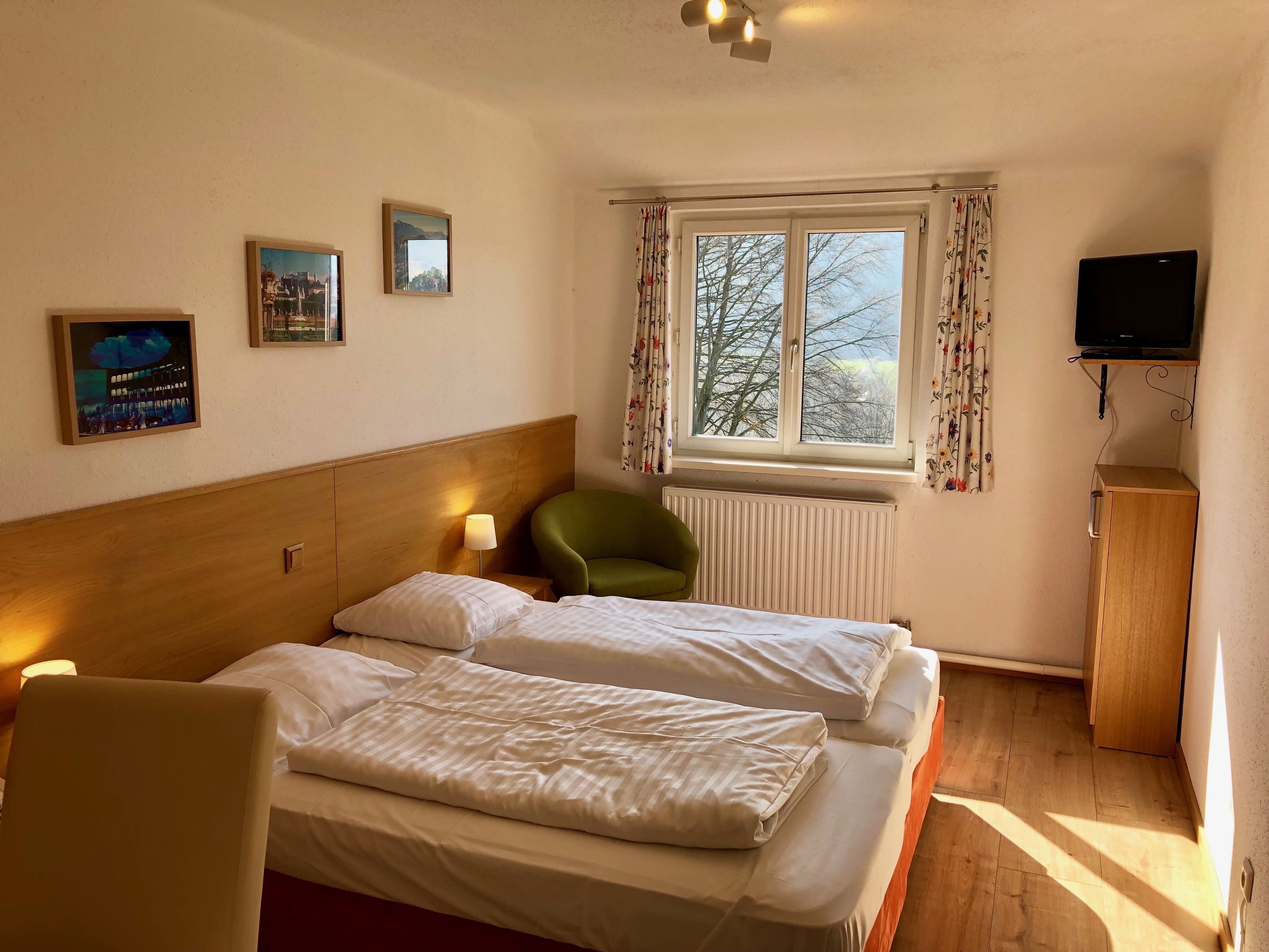 Habitación de hotel con dos camas, una silla verde, un televisor sobre un soporte y una ventana con cortinas.