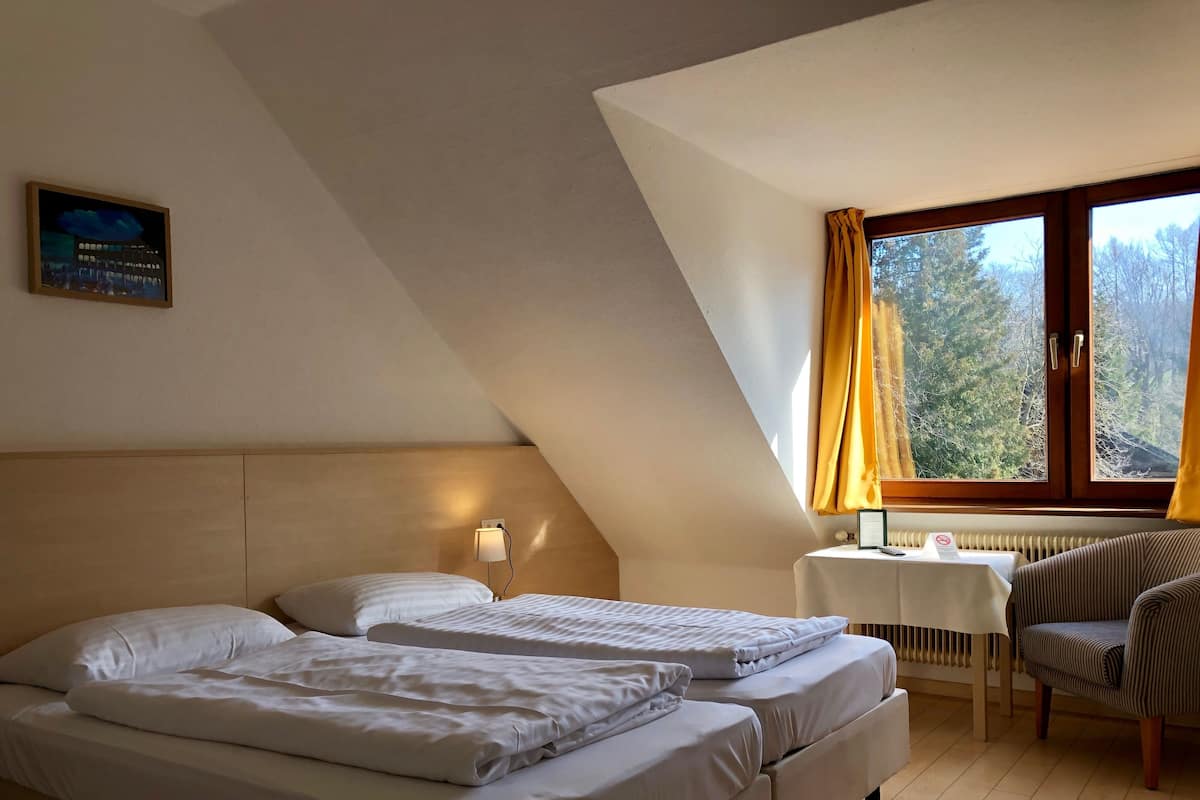 A hotel room with two beds, a desk, a chair, and a window with curtains.