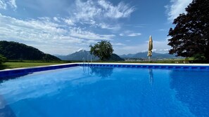 Una piscina con agua azul cristalina, rodeada de un césped cuidado y un gran árbol.