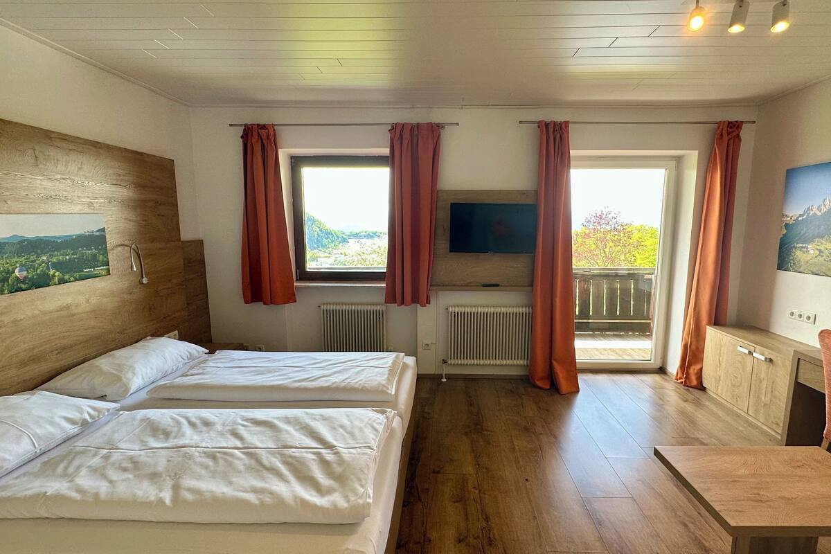 A hotel room with two beds, a TV, a desk, and a window with curtains.