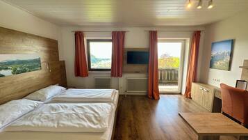 A hotel room with two beds, a TV, a desk, and a window with curtains.
