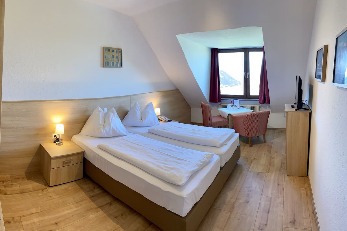 A modern hotel room with a large bed, a desk, and a window with a view of the mountains.