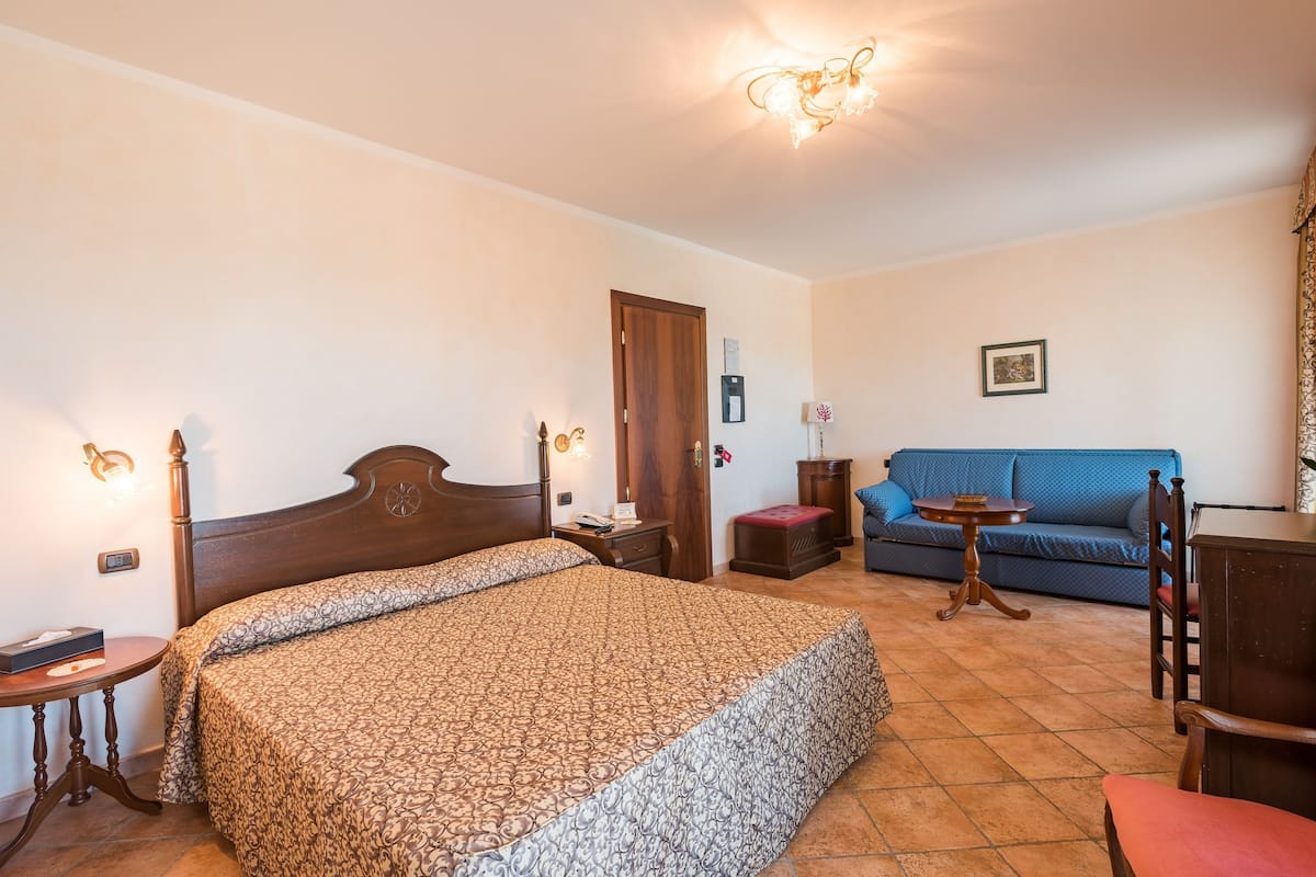 Ein Schlafzimmer mit einem großen Bett, einem Holzkopfende, einem Nachttisch, einem Beistelltisch, einem blauen Sofa, einem kleinen runden Tisch und einem Holzstuhl.