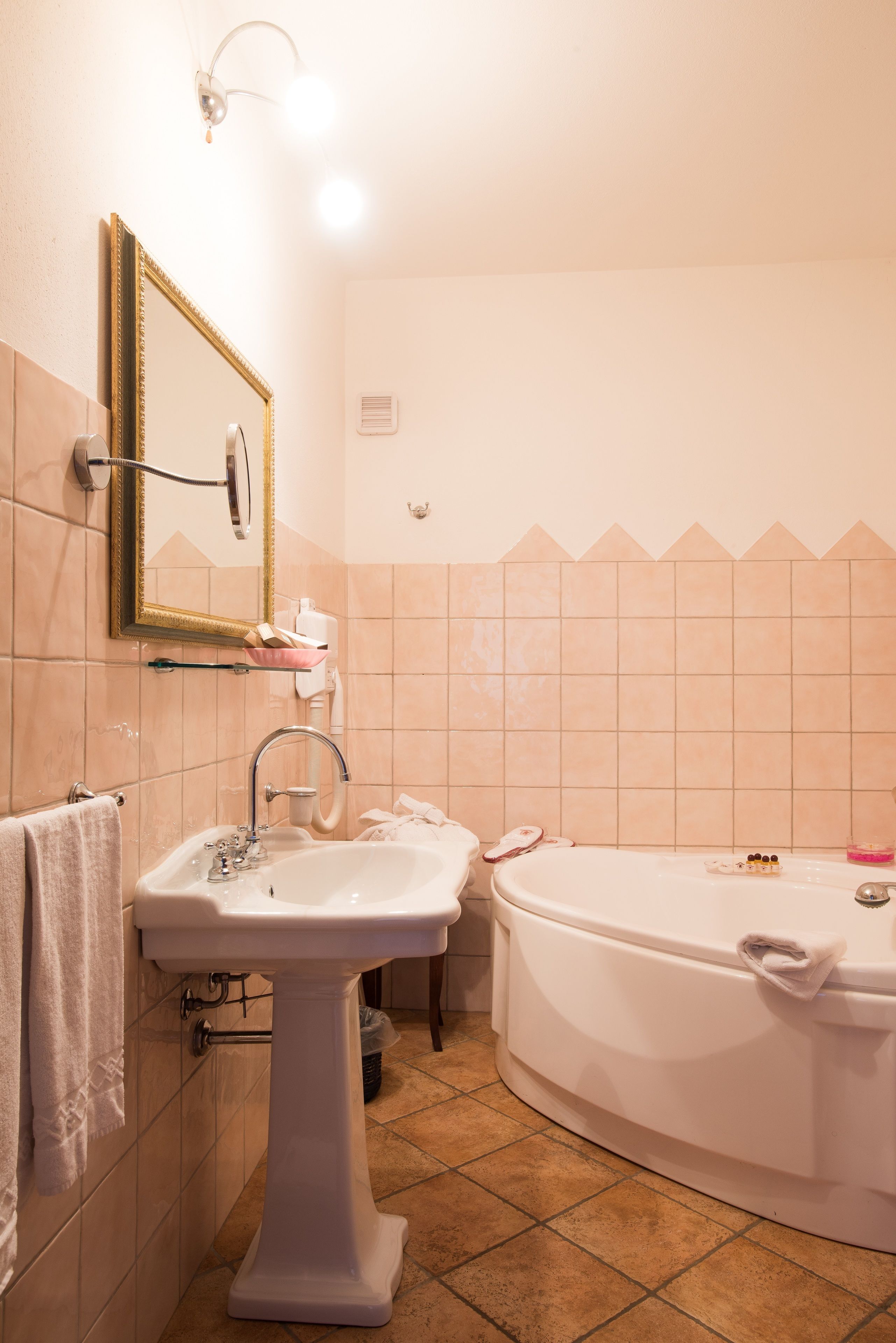 A bathroom with a pedestal sink, a large bathtub, and a wall-mounted mirror.