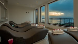 Un spa con sillones de masaje, toallas con pétalos de rosa y vistas al mar a través de grandes ventanales.
