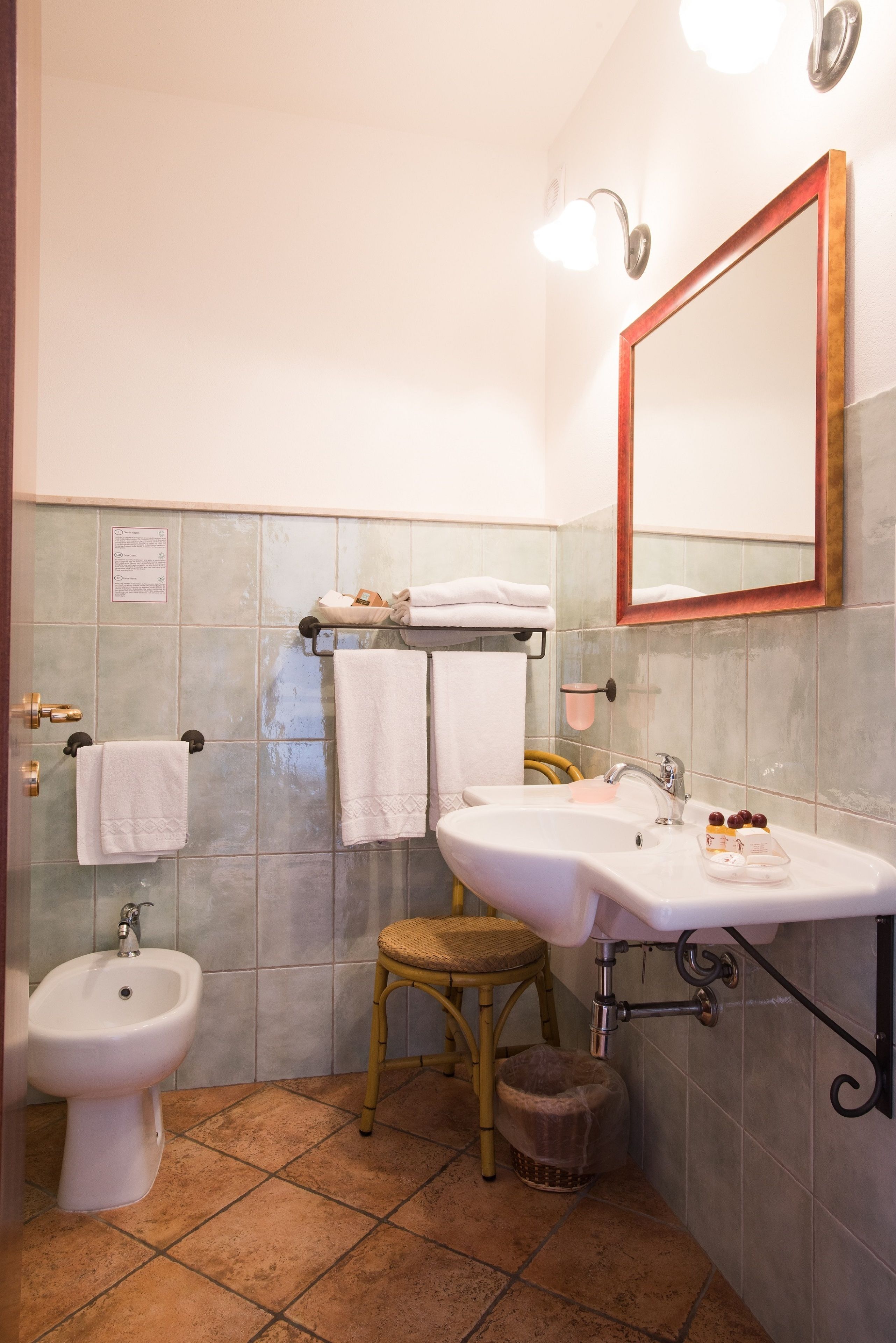 A bathroom with a bidet, sink, and mirror. There are towels on a rack and a wicker stool.