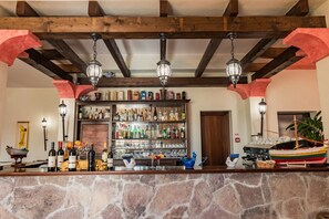 A bar area with a stone countertop, wooden beams, hanging lanterns, and a variety of bottles and glasses.
