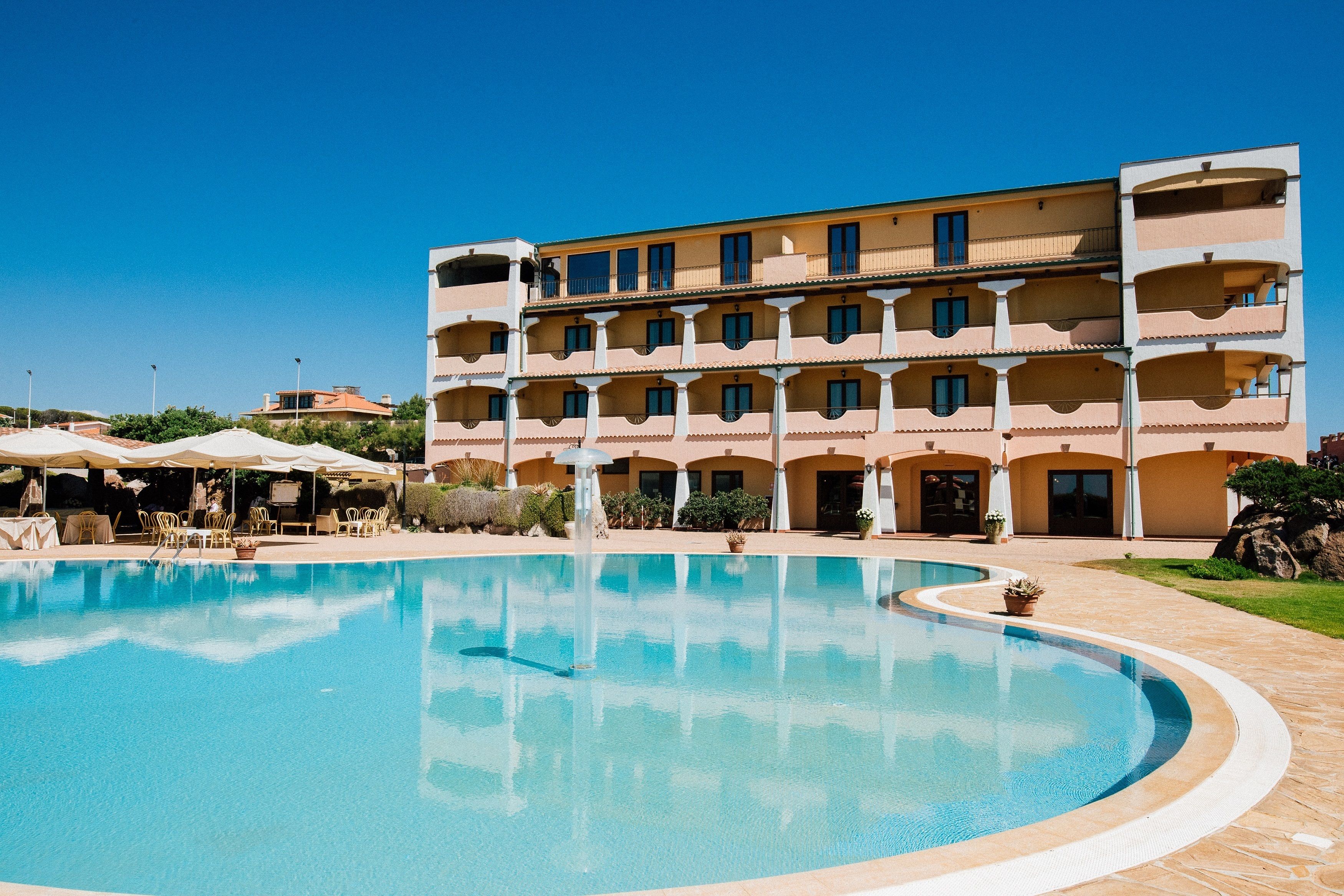 A hotel with a large swimming pool, multiple balconies, and outdoor seating areas.