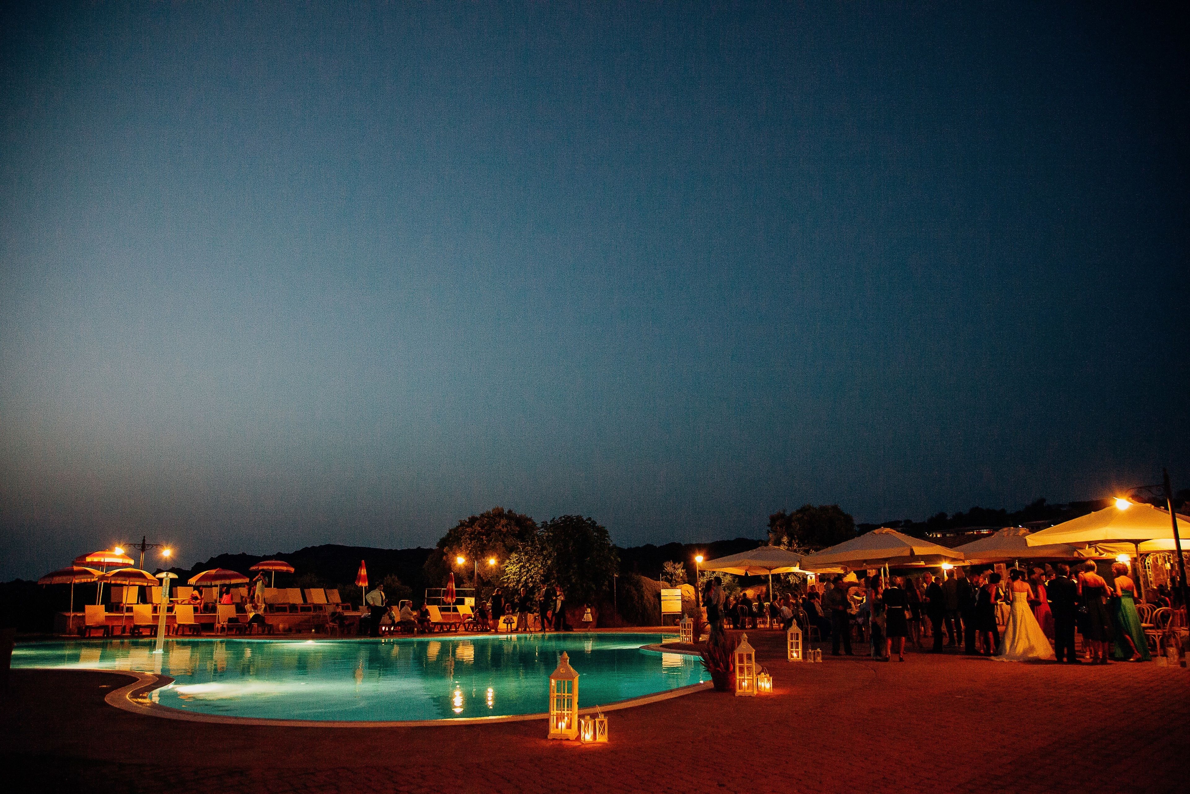 A pool area with lounge chairs and umbrellas, surrounded by a crowd of people.