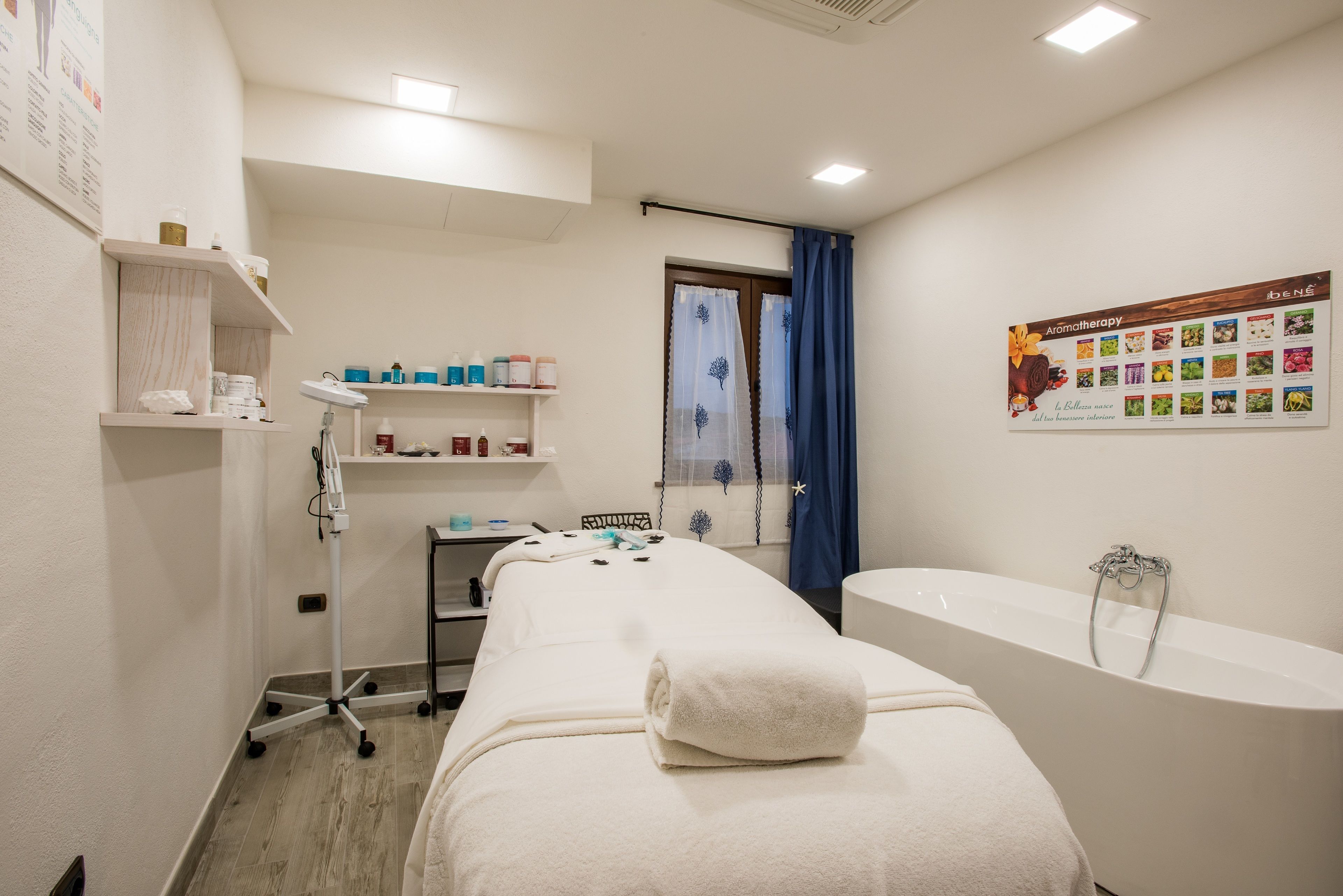 A spa room with a massage table, a bathtub, shelves with toiletries, and a poster on the wall.