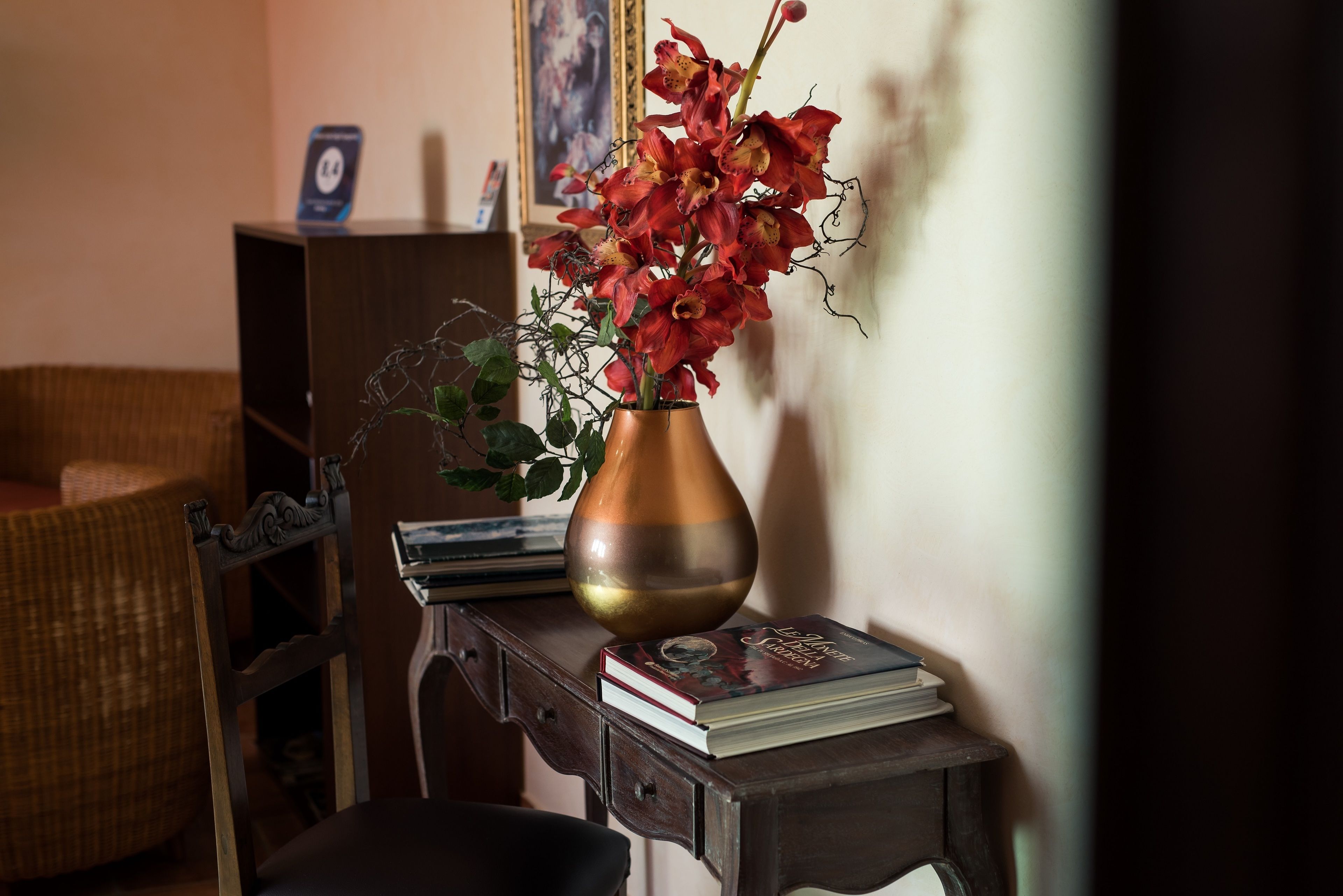 A wooden side table with a vase of red flowers and a book.