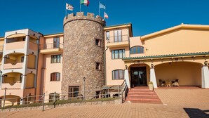 Un hotel con una torre central de piedra, varios balcones y una zona de entrada cubierta.