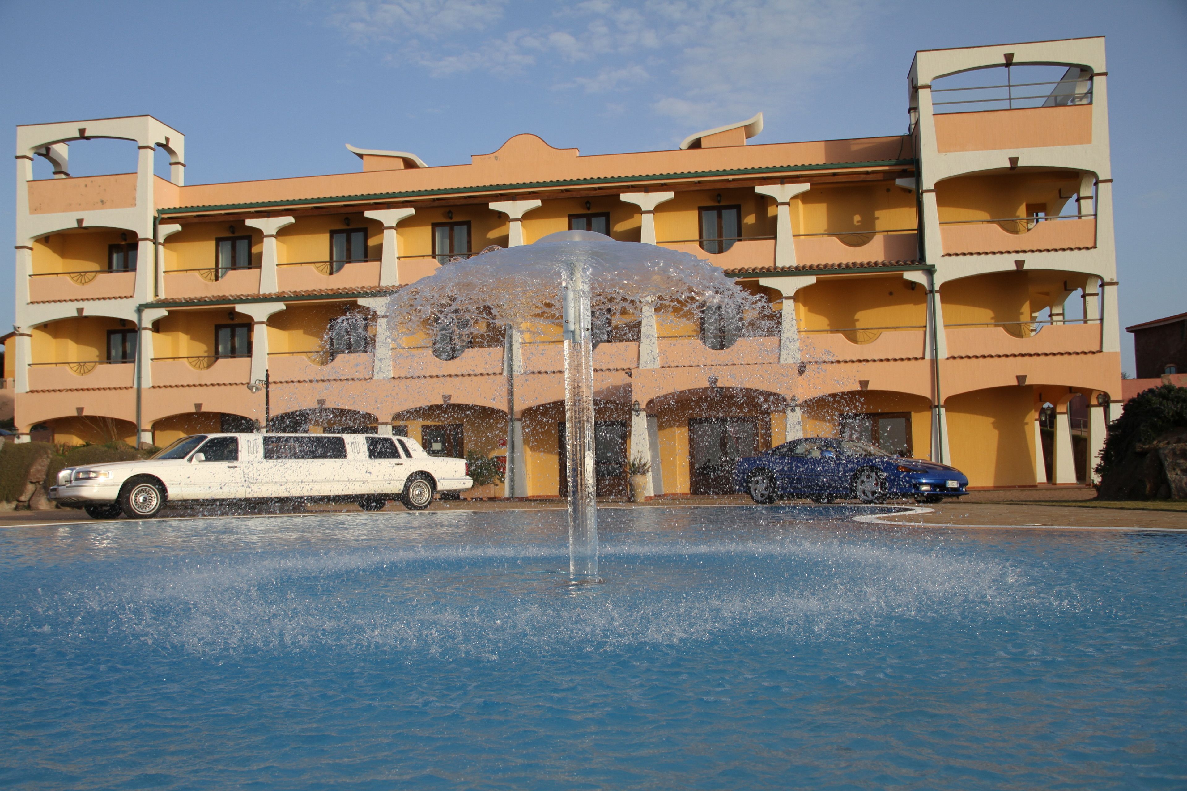 Un hotel con piscina, una fuente y un coche blanco y azul estacionado adelante.