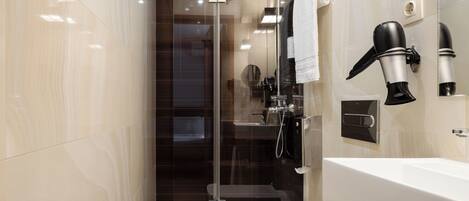 A modern bathroom with a glass-enclosed shower, a white bathtub, and a hairdryer mounted on the wall.