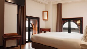 Une chambre d’hôtel avec un grand lit, une table de chevet en bois, un miroir et une vue sur l’extérieur grâce à une porte vitrée.