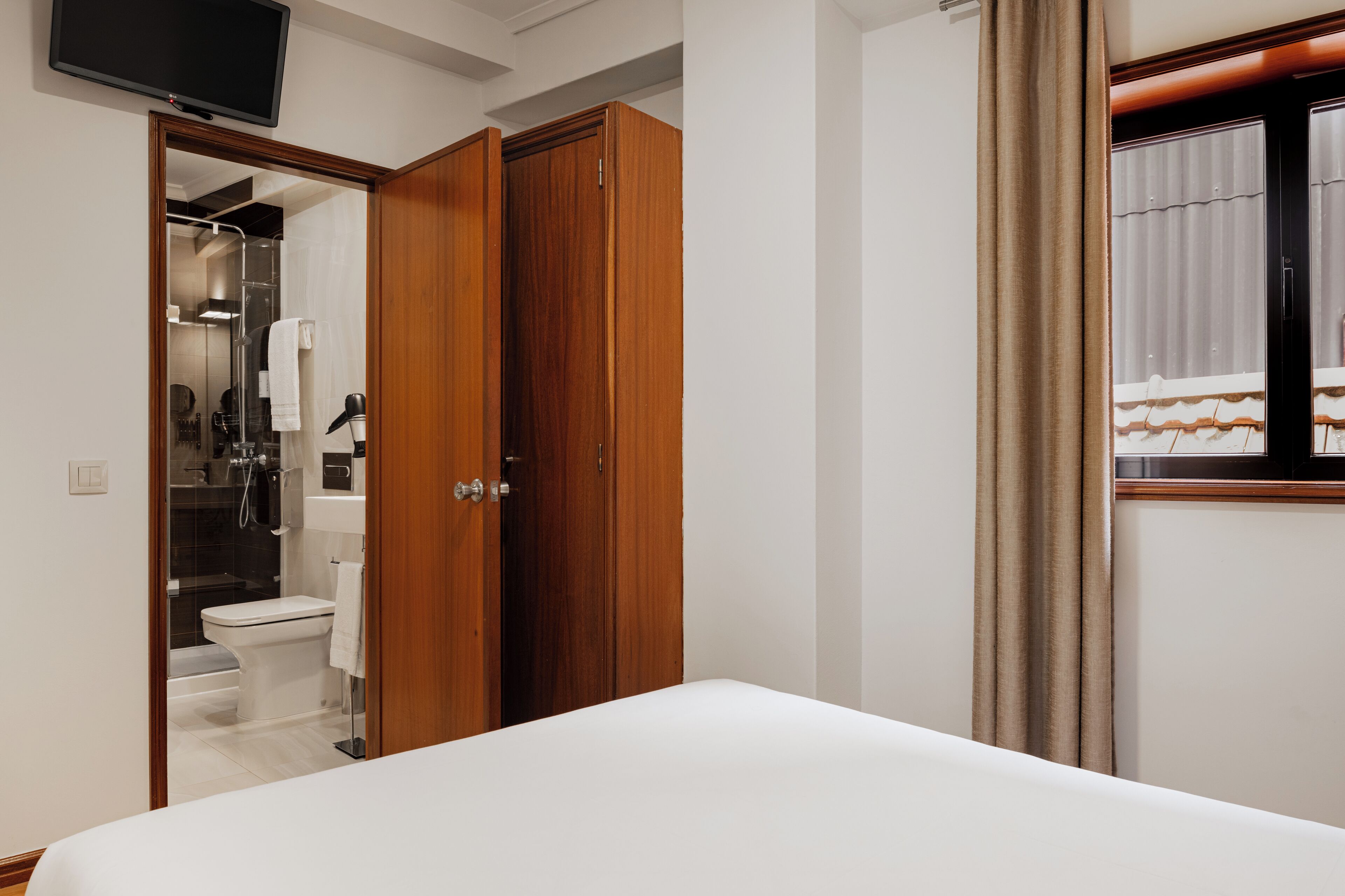 Habitación de hotel con cama, armario de madera, televisión y baño visible a través de una puerta abierta.