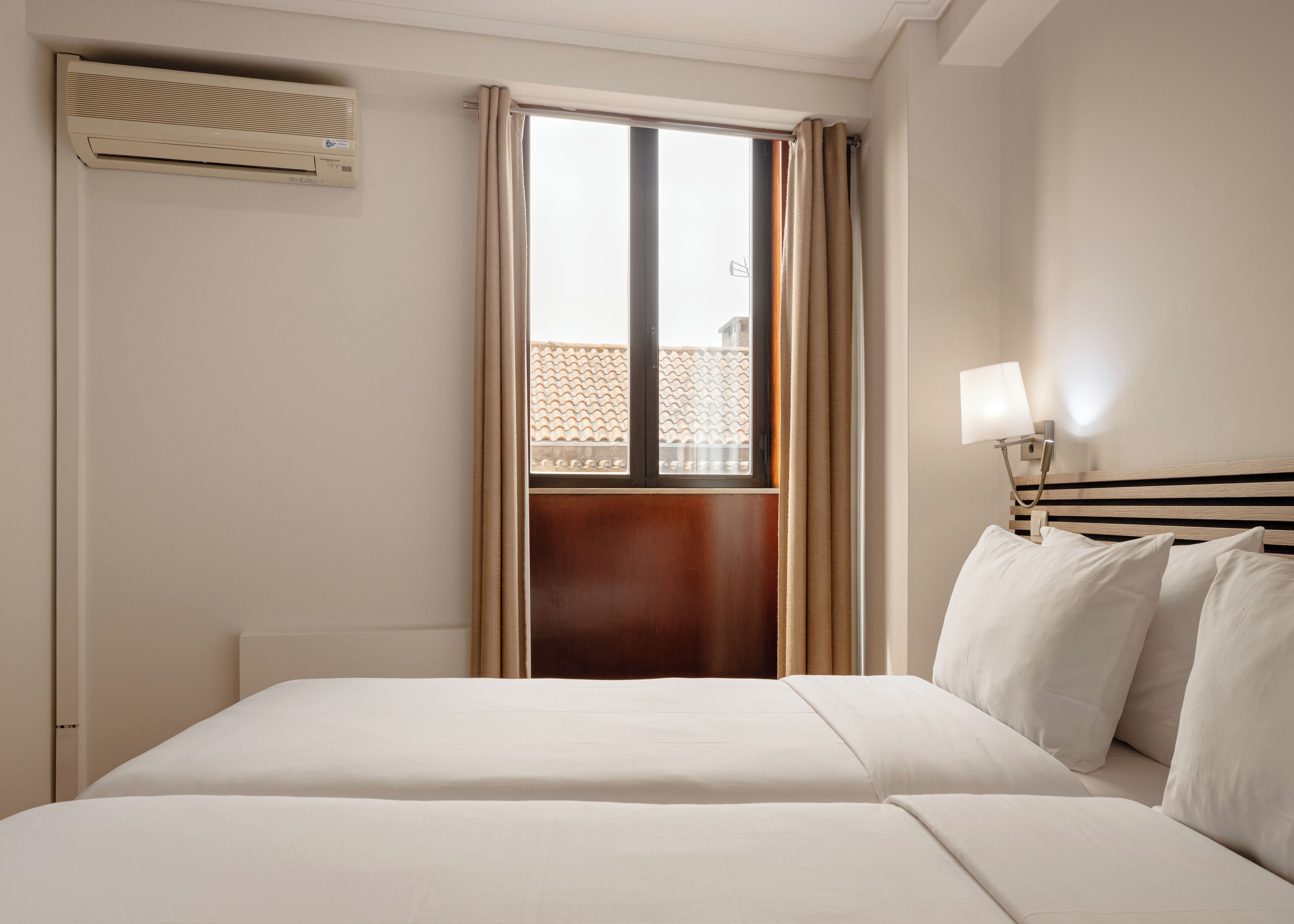 Ein Hotelzimmer mit Bett, Fenster mit Vorhängen, Wandklimaanlage und Nachttischlampe.