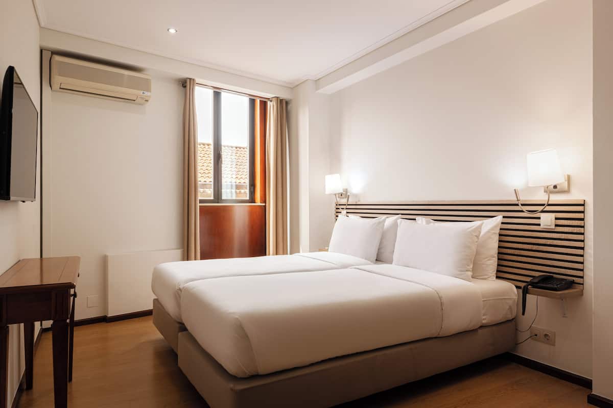 A hotel room with a large bed, a desk, a TV, and a window with curtains.