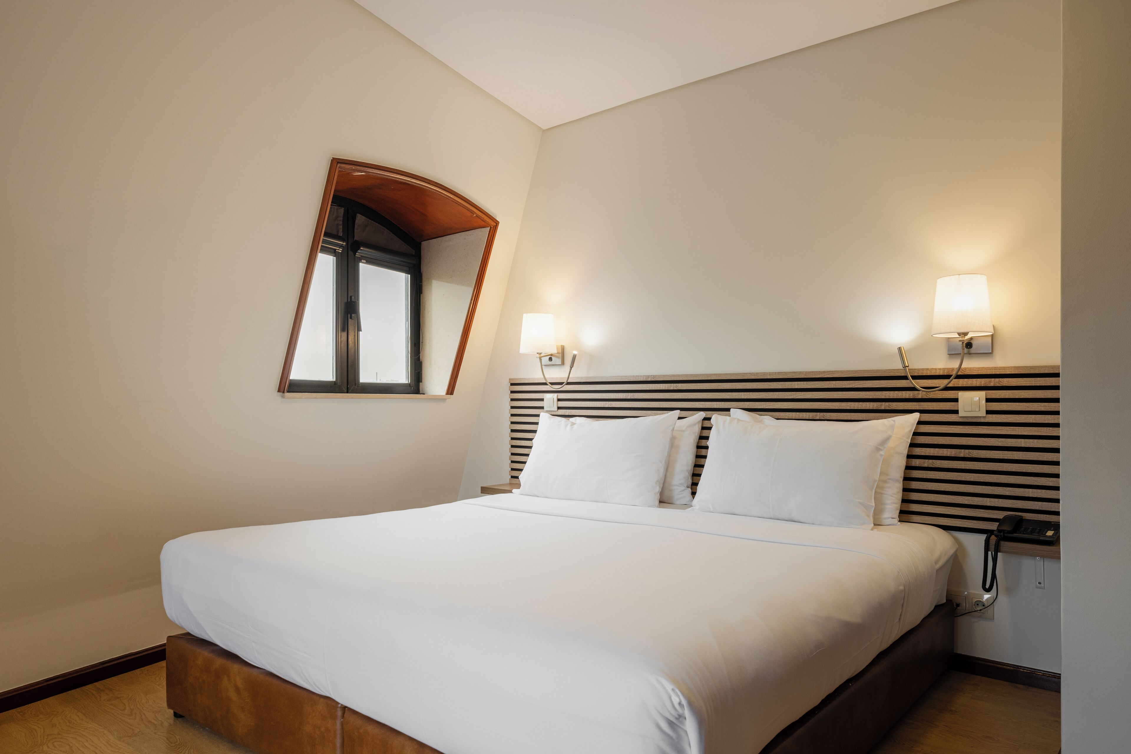 A neatly made bed with white linens, a wooden headboard, and two bedside lamps.