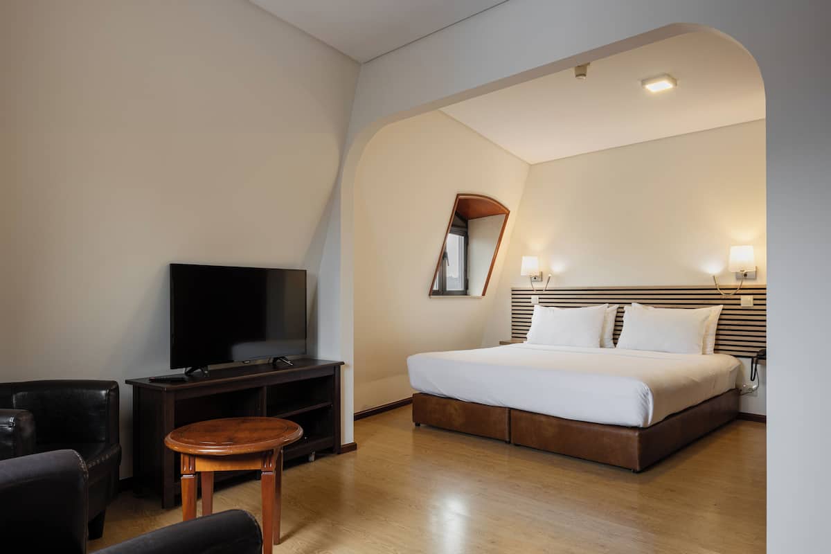 A hotel room with a large bed, a TV, a wooden coffee table, and a small round table.