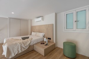 Ein modernes Schlafzimmer mit Bett, Nachttisch, grünem Hocker und einem Fenster mit Milchglas.