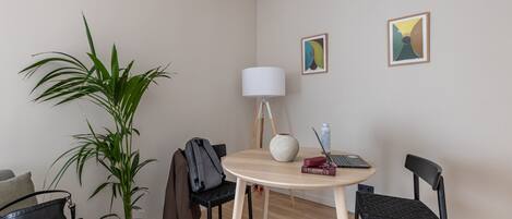 Une pièce moderne avec une table ronde en bois, deux chaises noires, une plante en pot, une lampe et deux œuvres d’art encadrées accrochées au mur.