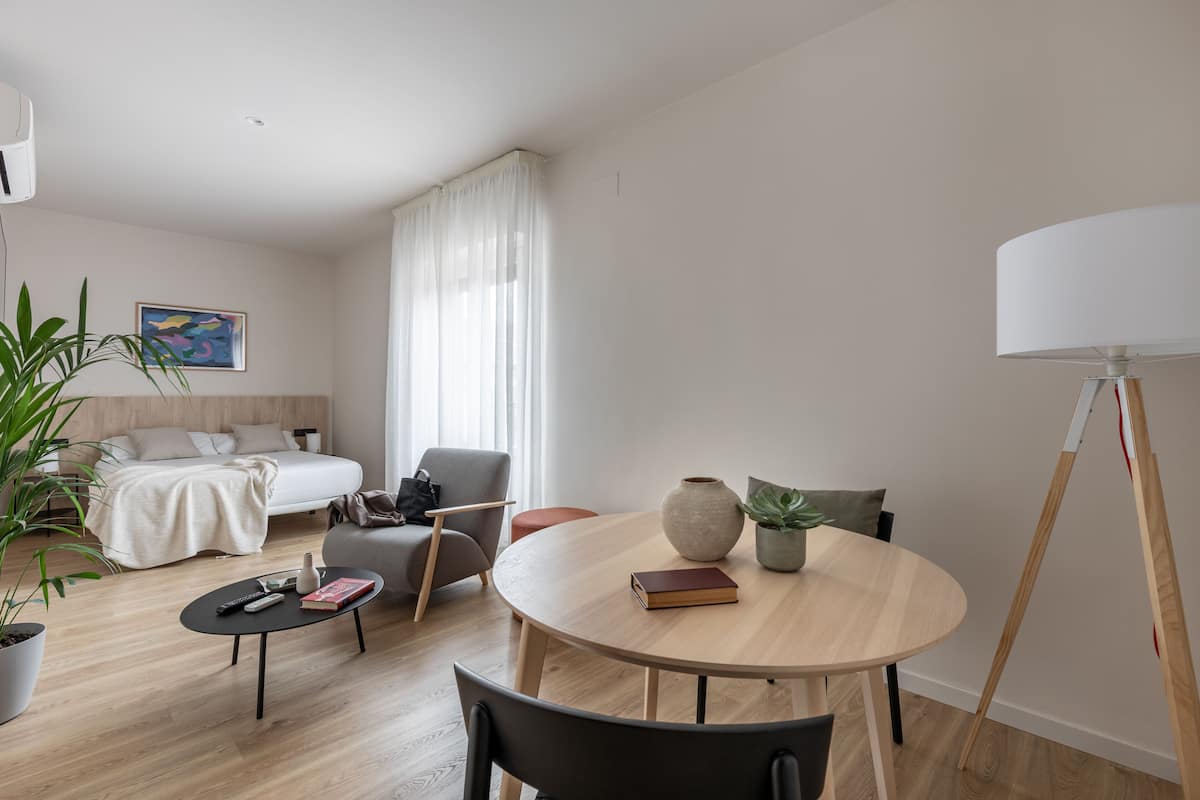 A modern, well-lit room with a bed, a sofa, a round table, and a lamp.
