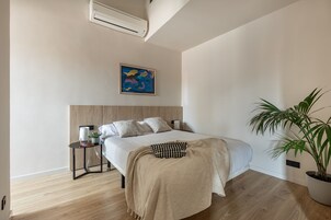 Ein modernes Schlafzimmer mit einem großen Bett, einem Nachttisch mit Lampe, einem kleinen Topfpflanzen und einem Bild an der Wand.
