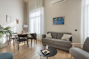 Ein modernes Wohnzimmer mit einem grauen Sofa, einem runden Couchtisch und einem Essbereich mit Tisch und Stühlen.